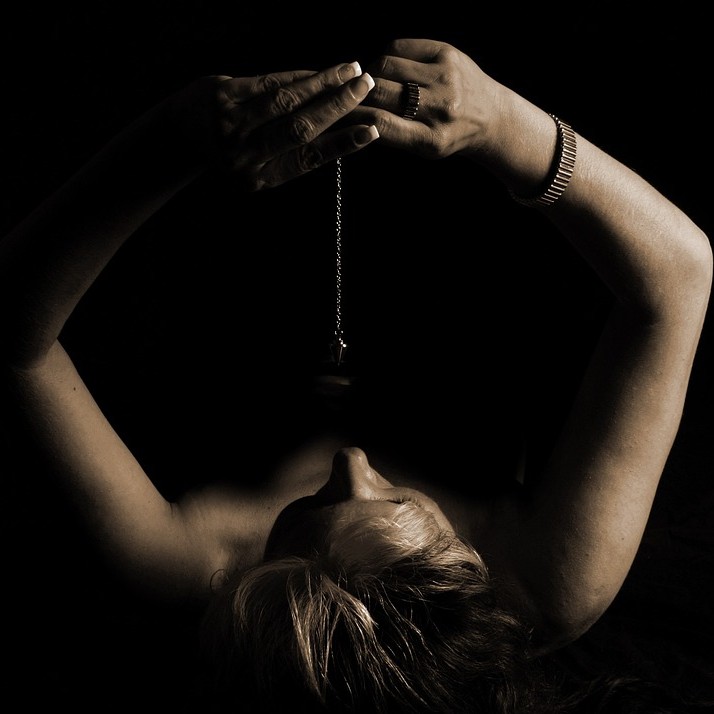 Auto-hipnose - mulher segurando um pêndulo em cima de si mesma